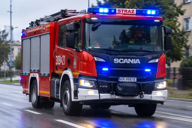 Red fire truck moving down the street, blurred lights and street traffic in the background