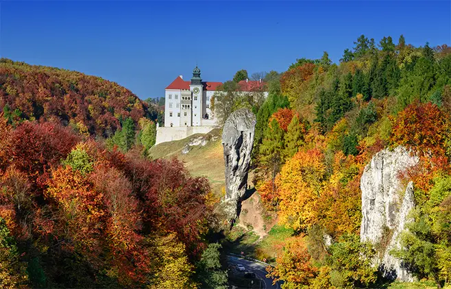 Pieskowa Skała Castle and Hercules' Club in Ojcowski National Park amidst autumn yellow-red trees.